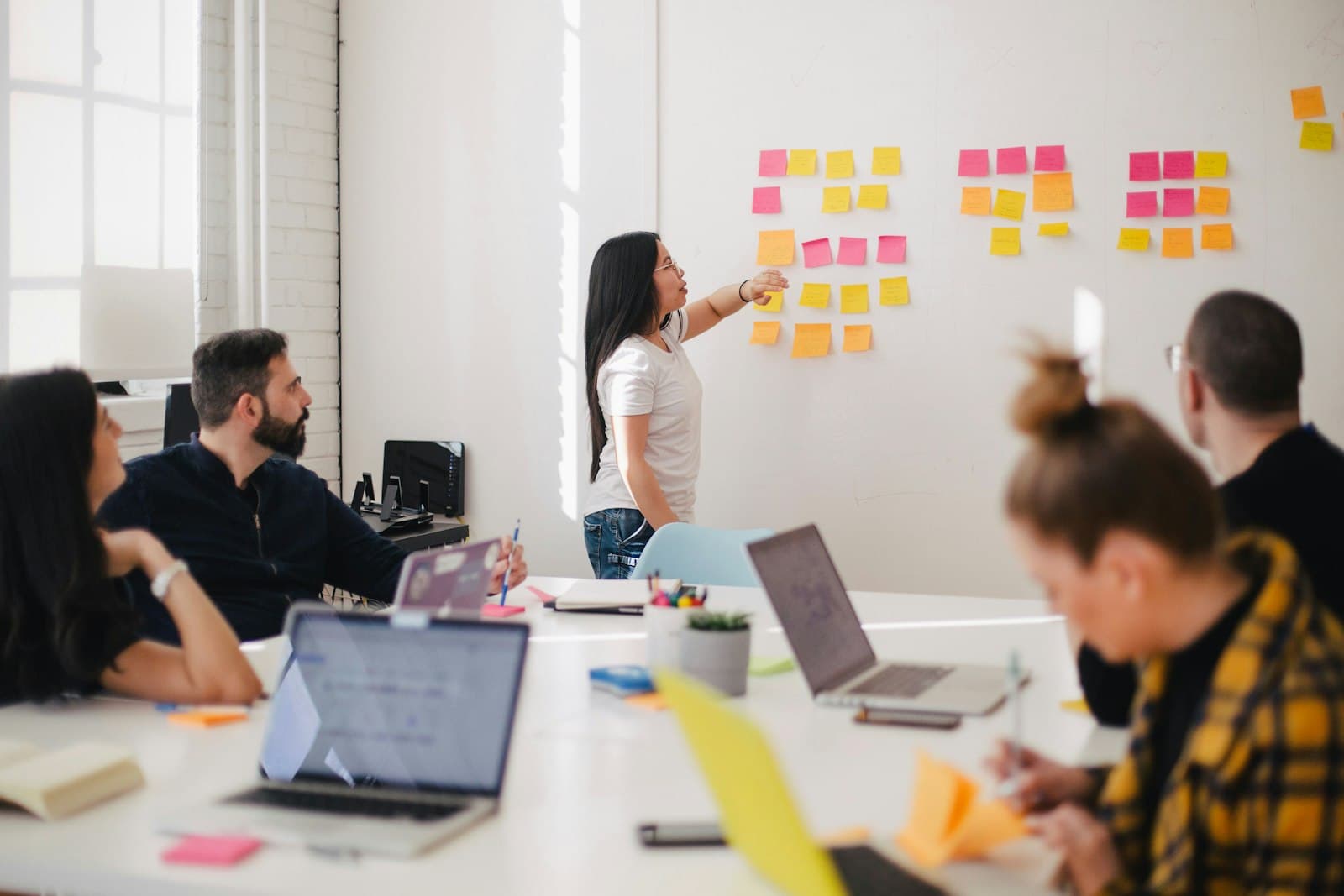 A consultant mapping workflow steps on a wall of sticky notes while the team looks on